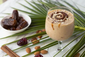 A top-down flat lay image of fresh, wholesome ingredients for a date palm smoothie, including Medjool dates, a banana, milk, ice cubes, cinnamon, and almonds, beautifully arranged on a light-colored surface
